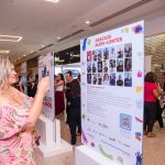 Mulher loira segura celular e fotografa um dos totens da exposição Aracaju Além das Lentes